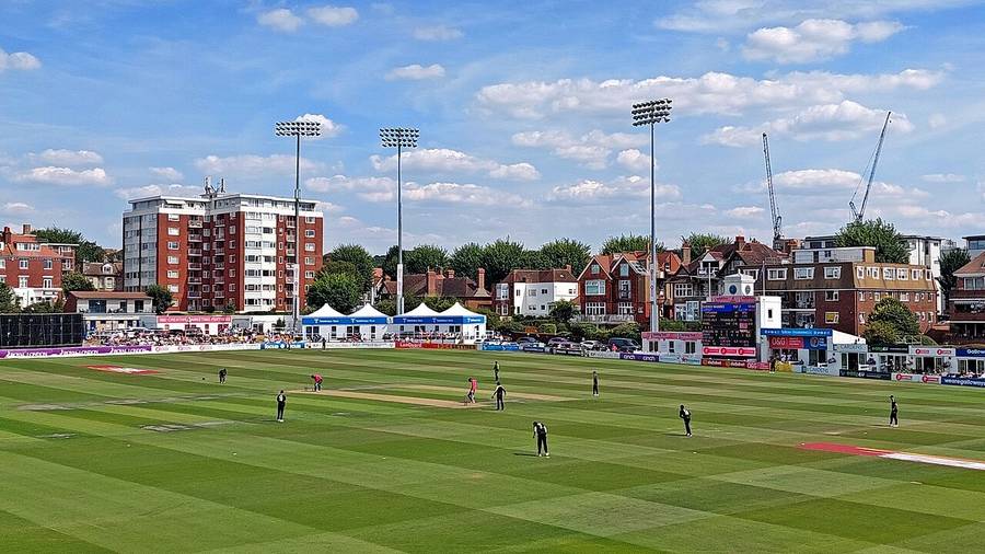 Players in the field during a match at the County Ground, Hove, with floodlights and flats behind the boundary