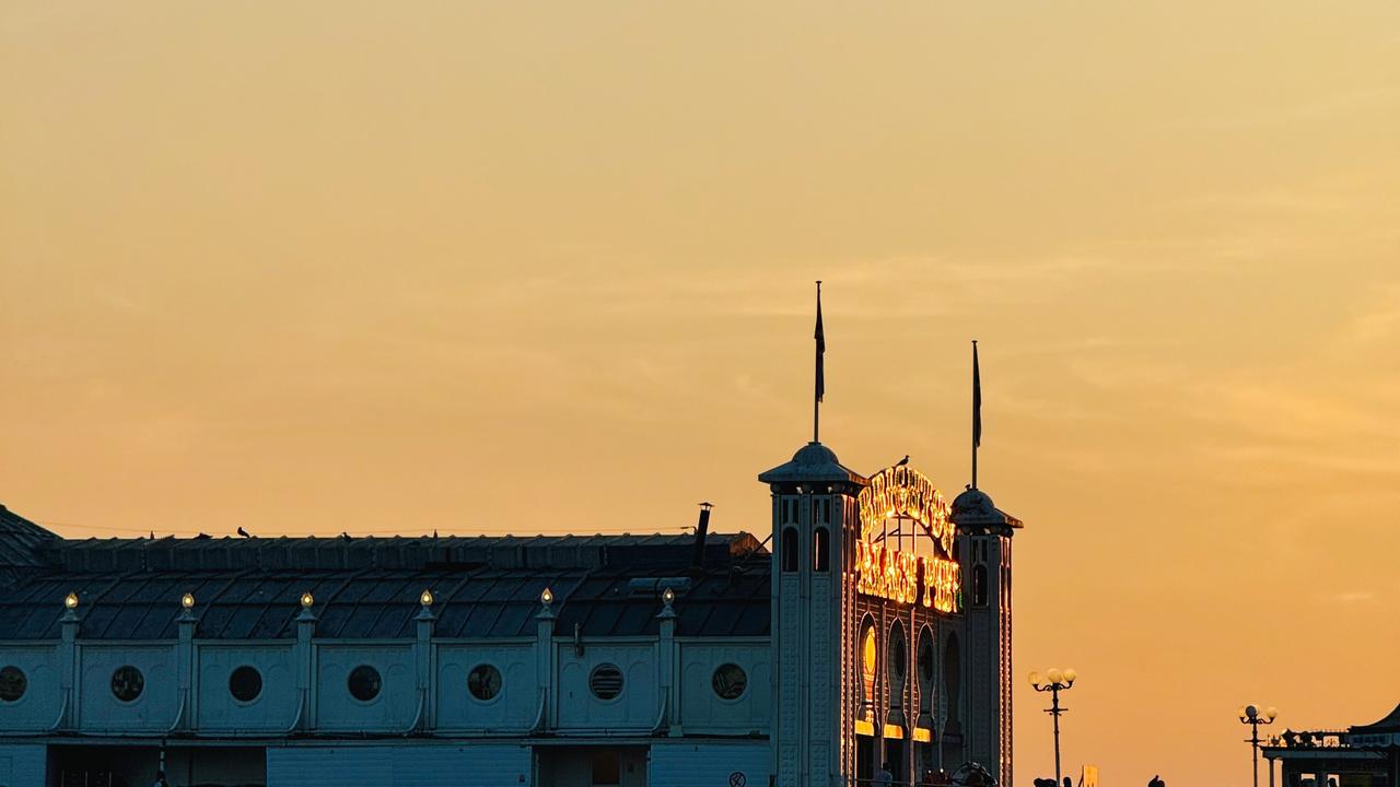 The roof and domed towers of Brighton’s Palace Pier lit against an orange sunset sky