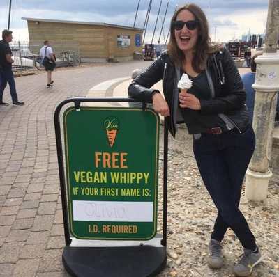 OffersOn founder Olivia Gray laughing while holding an ice cream beside a free vegan whippy sign on Brighton seafront