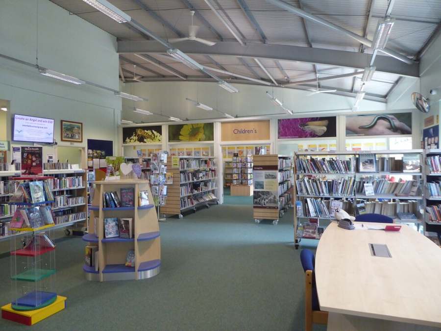 Inside Patcham Library, with bookshelves, a children’s section sign and a large study table under a high roof