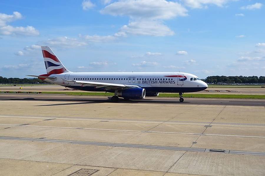 A British Airways Airbus A320 taxiing along a runway at Gatwick Airport under a blue sky with white clouds