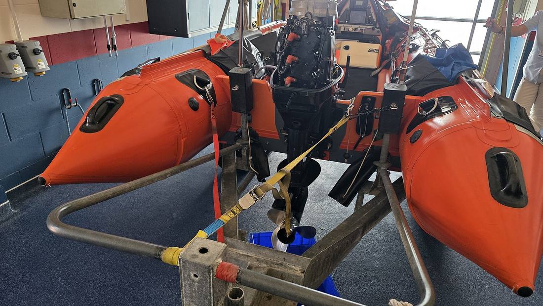 The orange bow of an RNLI inshore lifeboat with its outboard engine, on its launching carriage inside the Shoreham Harbour lifeboat station
