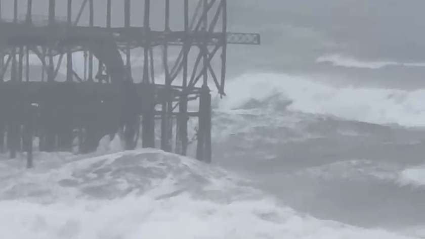 Large grey waves breaking around the iron legs at the base of the West Pier frame