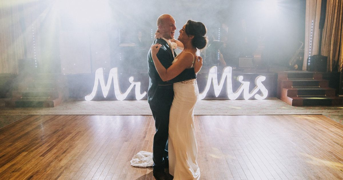 A couple dancing beside a light-up Mr and Mrs sign in a hazy ballroom