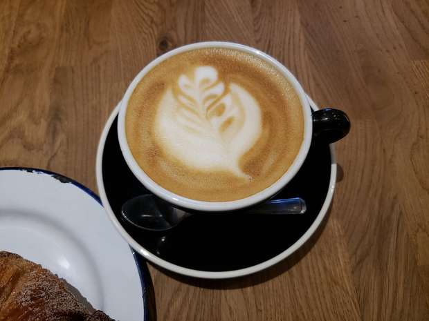 A latte with leaf-shaped milk art on a wooden table at a Brighton cafe
