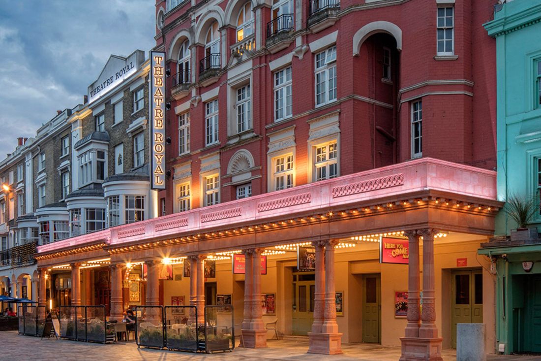 The red-brick front of the Theatre Royal Brighton on New Road at dusk, with its illuminated sign and covered entrance