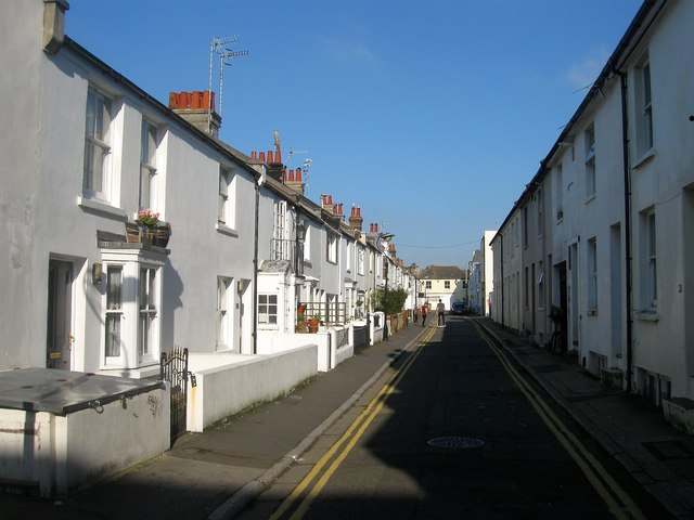 A narrow Brighton street of white terraced houses with double yellow lines, looking towards a distant building