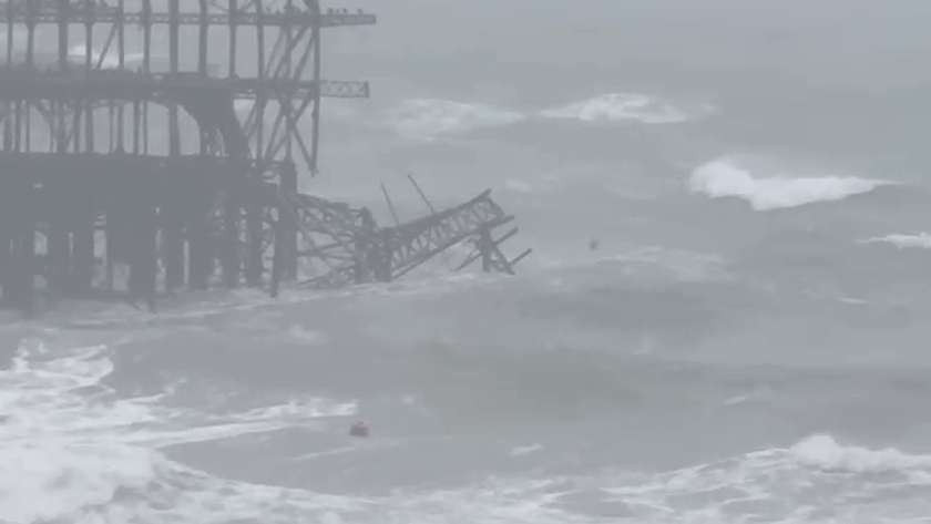 Wide view of the West Pier frame in grey sea with a tilted collapsed section hanging off its right side