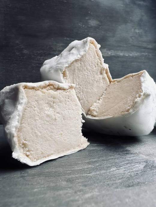Pieces of soft white vegan cheese with a bloomy rind on a dark slate surface