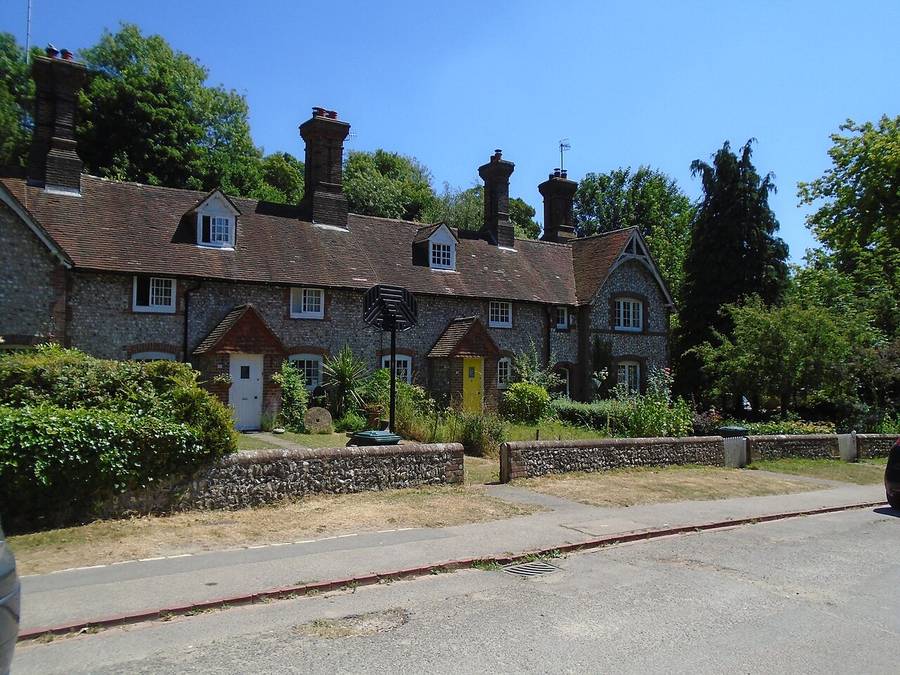 A row of flint cottages with tiled roofs and tall chimneys in Stanmer village under a blue sky