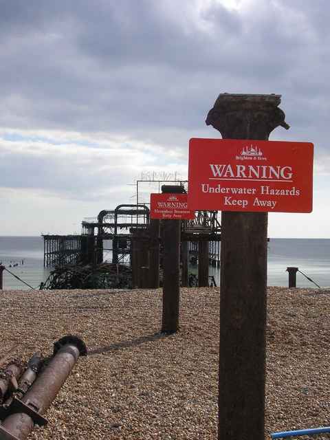 Warning signs on the beach with the West Pier ruin behind