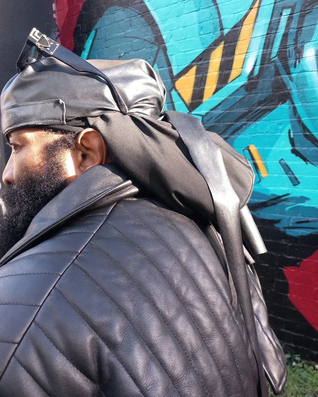 Charles Pirate Saddler in a black leather outfit and headwrap, side profile against a Brighton graffiti wall